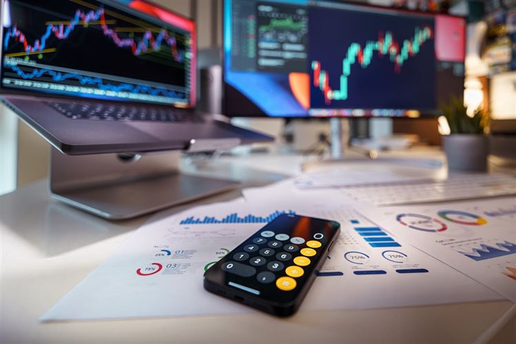 Datorer med grafer och en telefon med miniräknare symboliserar investering.