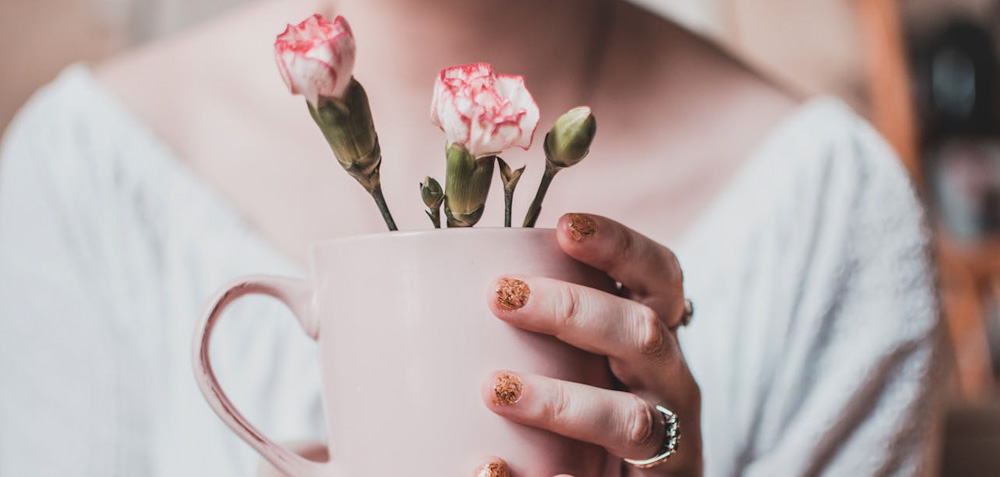 Kvinna som håller en rosa kaffekopp innehållandes rosa blommor